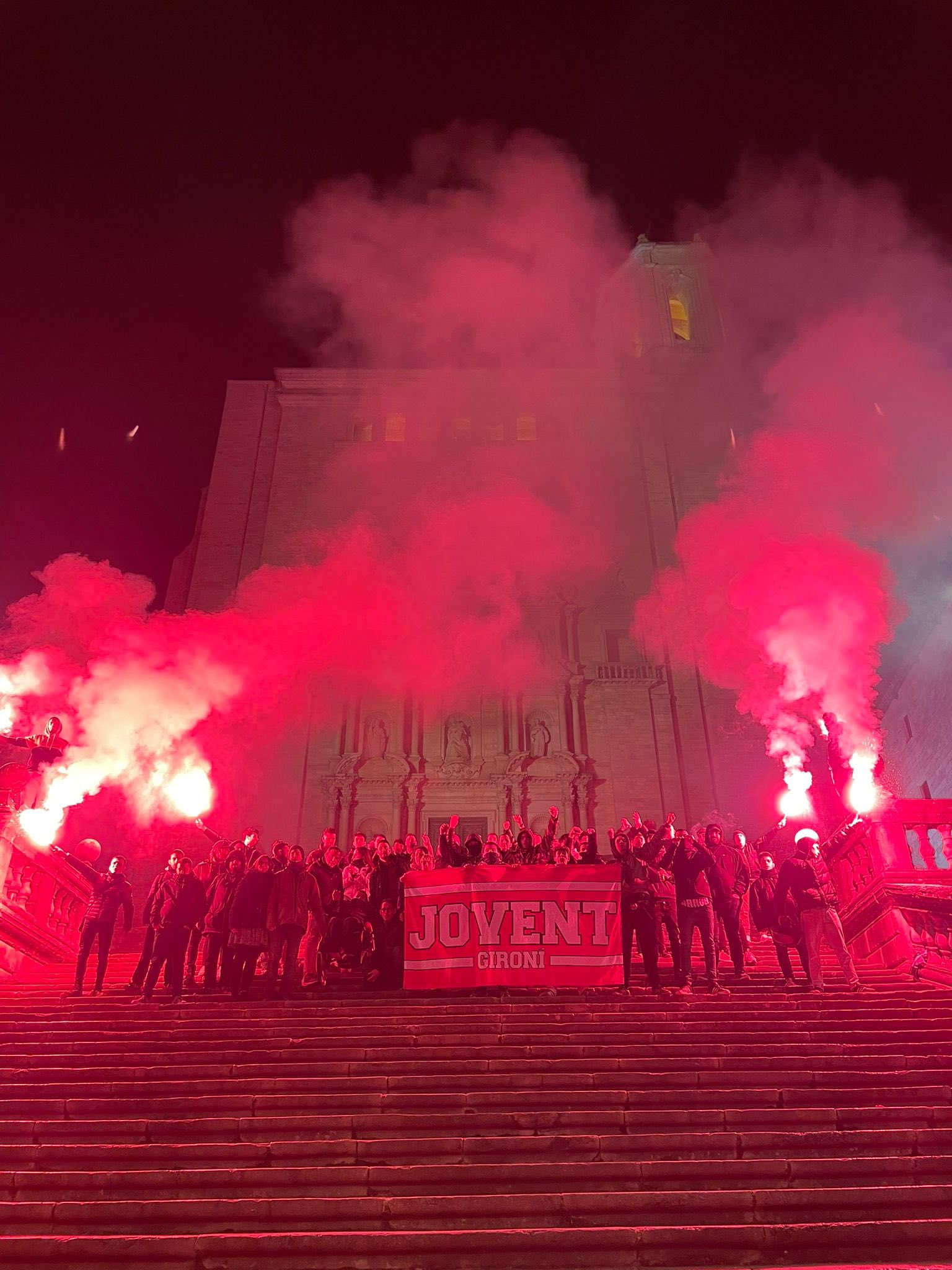 Jovent Gironí amb la bandera i bengales enceses tenyint de vermell el paissatge davant la catedral de Girona.