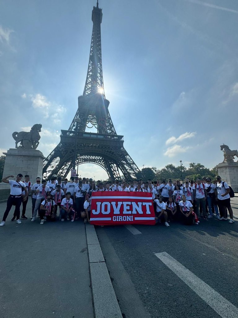 Jovent Gironí davant la torre Eifel abans del partit contra el PSG, amb la bandera del Jovent i tots els membres duen una samarreta blanca de indumentaria i les bufandes del Jovent Gironí.